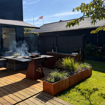 højbede i cortenstål og bålgrill i en have