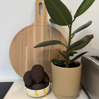 Rundt skærebræt med håndtag i køkken, med avokado i en skål foran