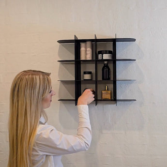 sort vægreol med små rum, til badeværelset  kvinde sætter parfume på plads